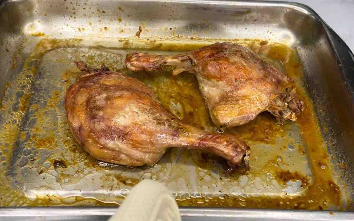 Two roasted duck legs on a baking pan, perfectly crisp and golden brown.