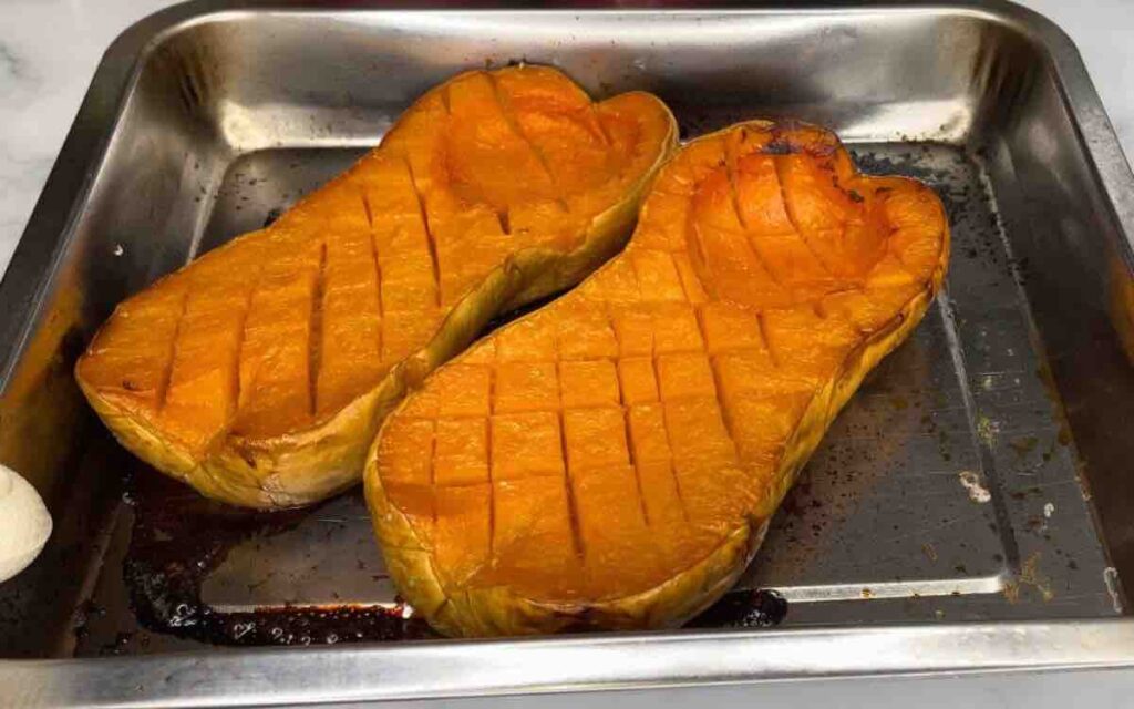 Two halves of butternut squash, roasted and golden brown, on a baking pan.