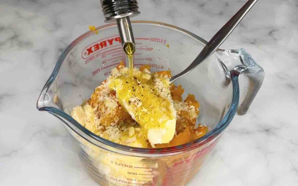 Medium-sized butternut squash, olive oil, kosher salt, ground black pepper, mascarpone cheese, and grated parmesan cheese in a clear bowl, ready to be blended smooth.