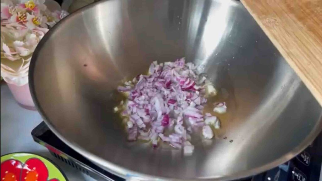 Chopped red onion cooking in a wok with olive oil.