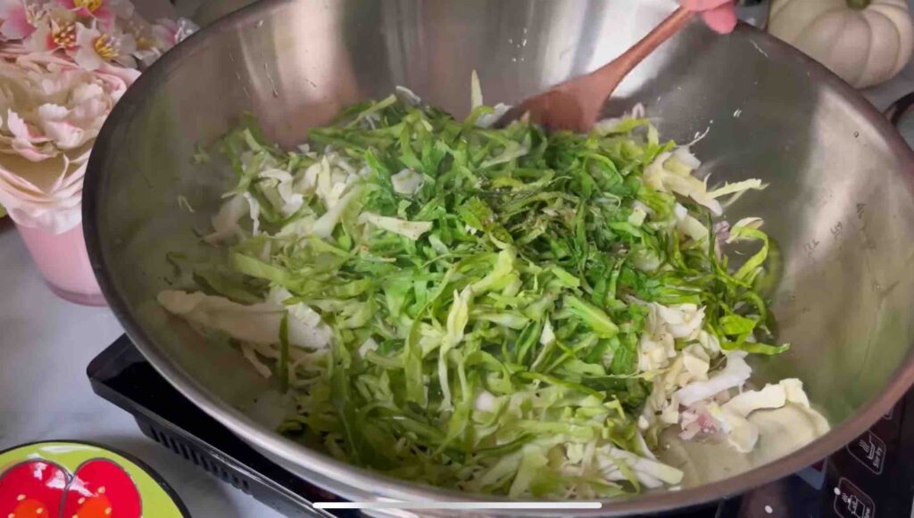 Chopped red onion sautéing in a wok with olive oil, with shredded cabbage being added for cooking.