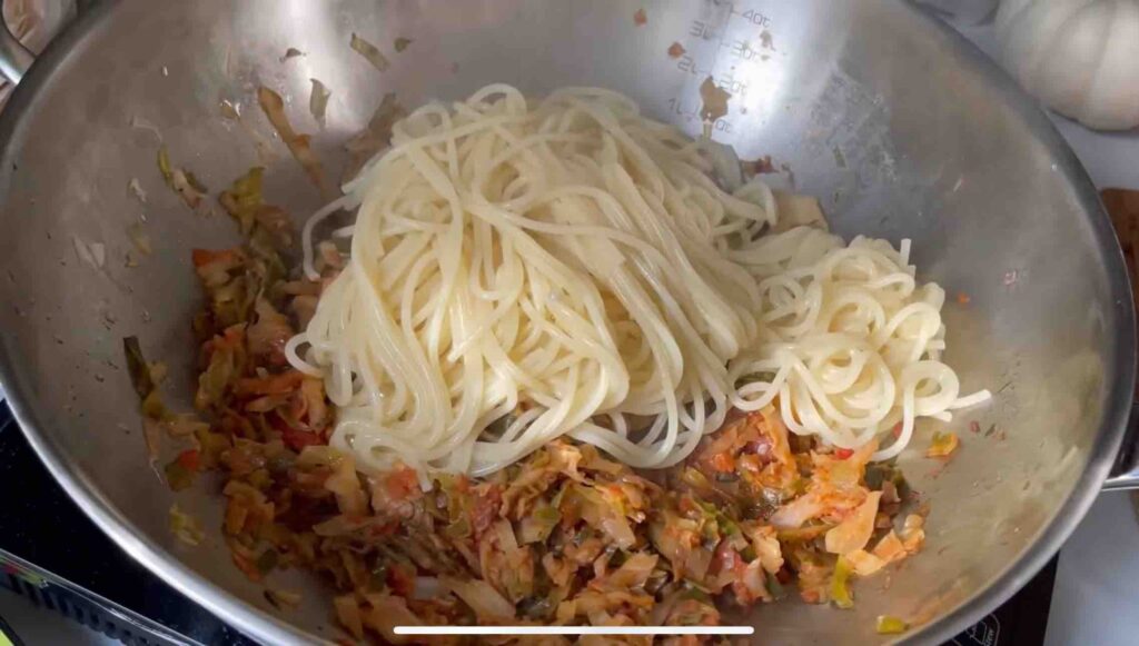 Chopped red onion cooking in olive oil in a wok, with shredded cabbage and tomato sauce, with cooked spaghetti being added.