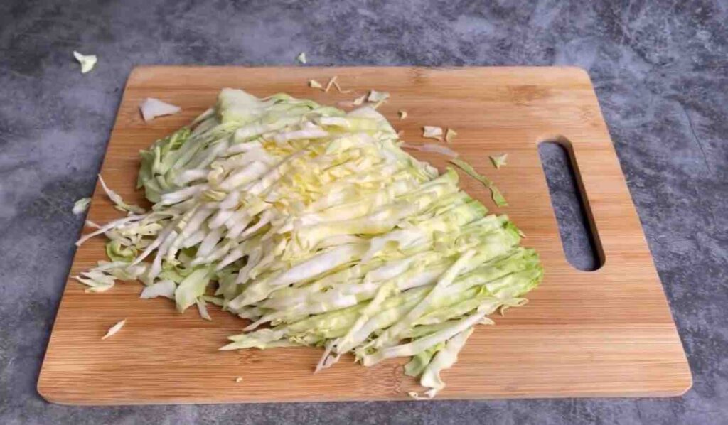 Half of a cabbage, shredded and spread out on a wooden cutting board.