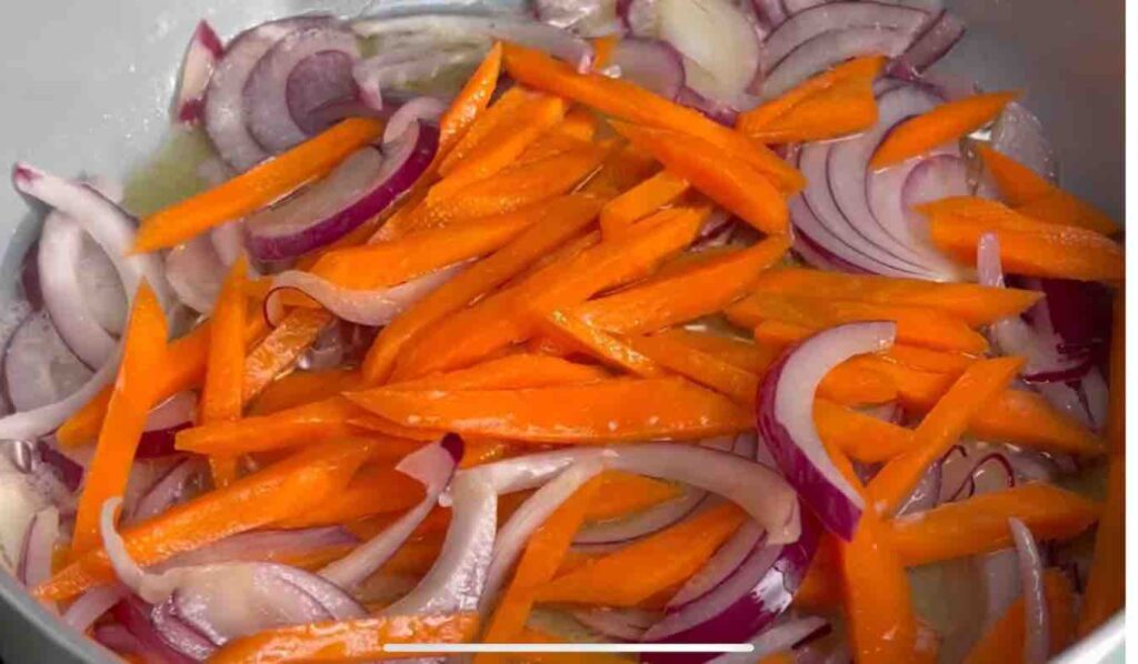 Sliced red onion and thinly sliced carrot cooking in a pan with olive oil and butter.