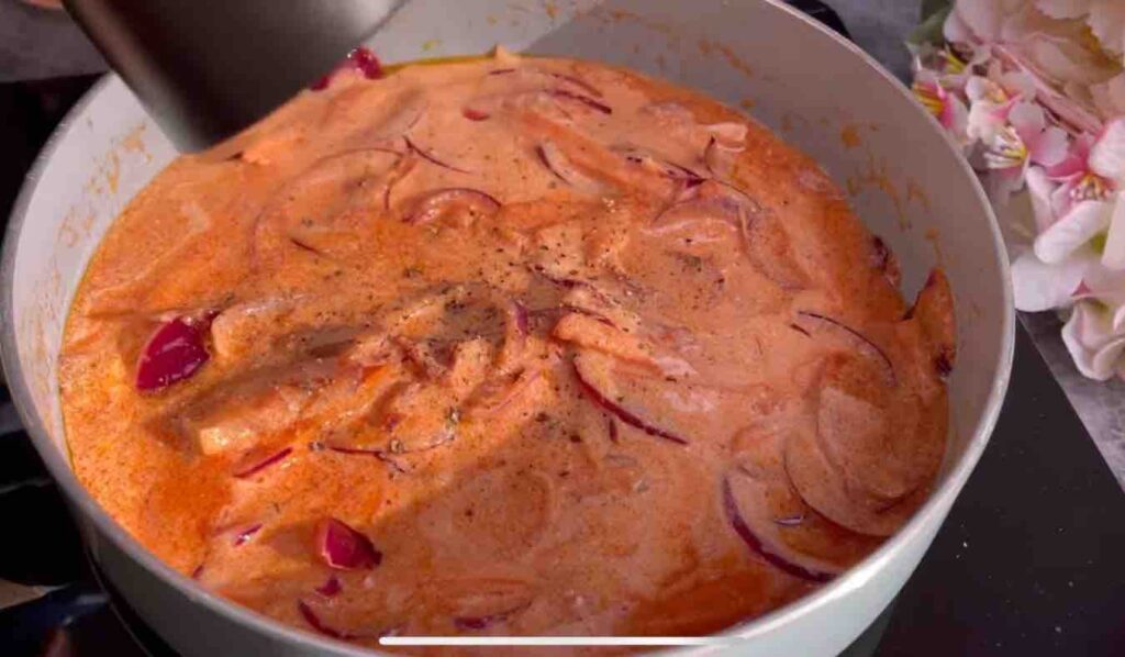 Red onion and carrot slices sautéed in olive oil and butter, with tomato sauce and sour cream added, cooking in a pan.