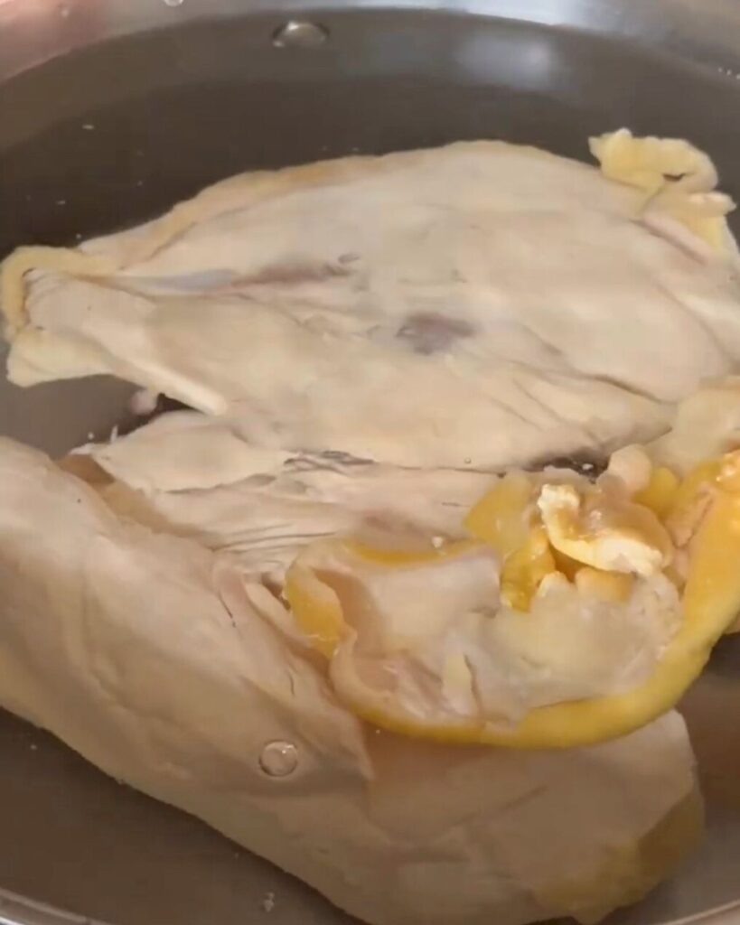 A raw chicken breast placed in a pan filled with water, ready to be cooked on the stovetop.