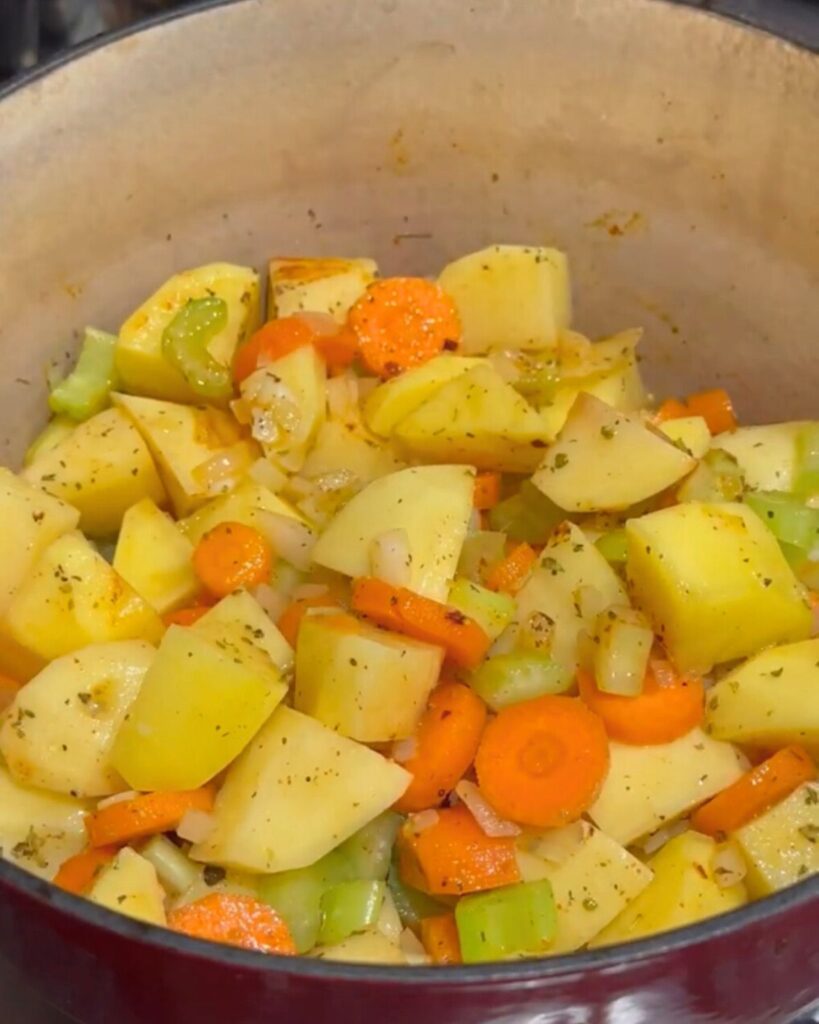 A deep pot filled with diced potatoes, carrots, onions, and sliced celery sticks, ready to be sautéed.