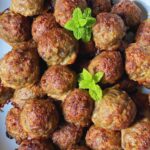 Baked meatballs in a ceramic white bowl decorated with mint leaves.