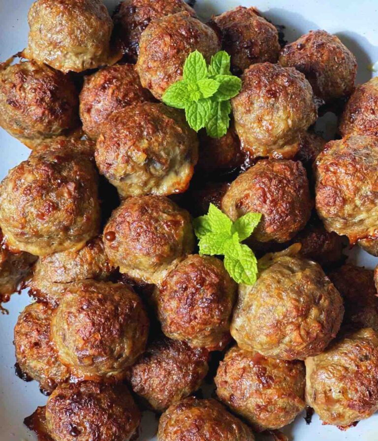 Baked meatballs in a ceramic white bowl decorated with mint leaves.