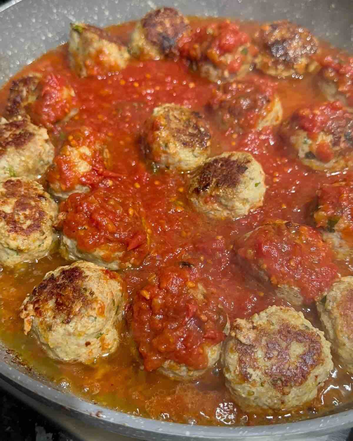 Meatballs simmering in a rich tomato sauce in a pan on the stove, bubbling gently as they cook.