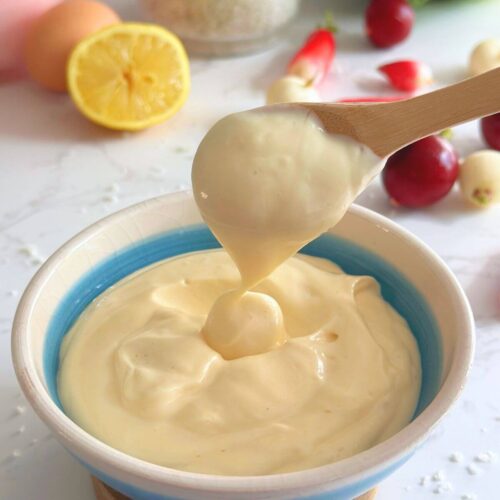 A bowl of homemade mayonnaise made with 4 ingredients, with a wooden spoon scooping up the creamy mayo to show its texture.