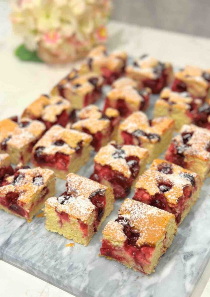 Squares of Morello Cherry Sponge Cake displayed on a marble surface, showcasing the moist center filled with juicy cherries.