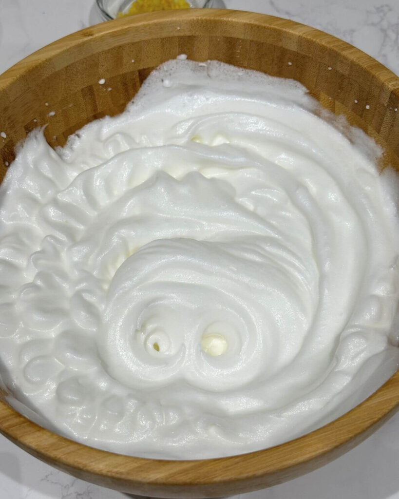 Egg whites beaten to stiff peaks in a wooden bowl, ready for making sponge cake.