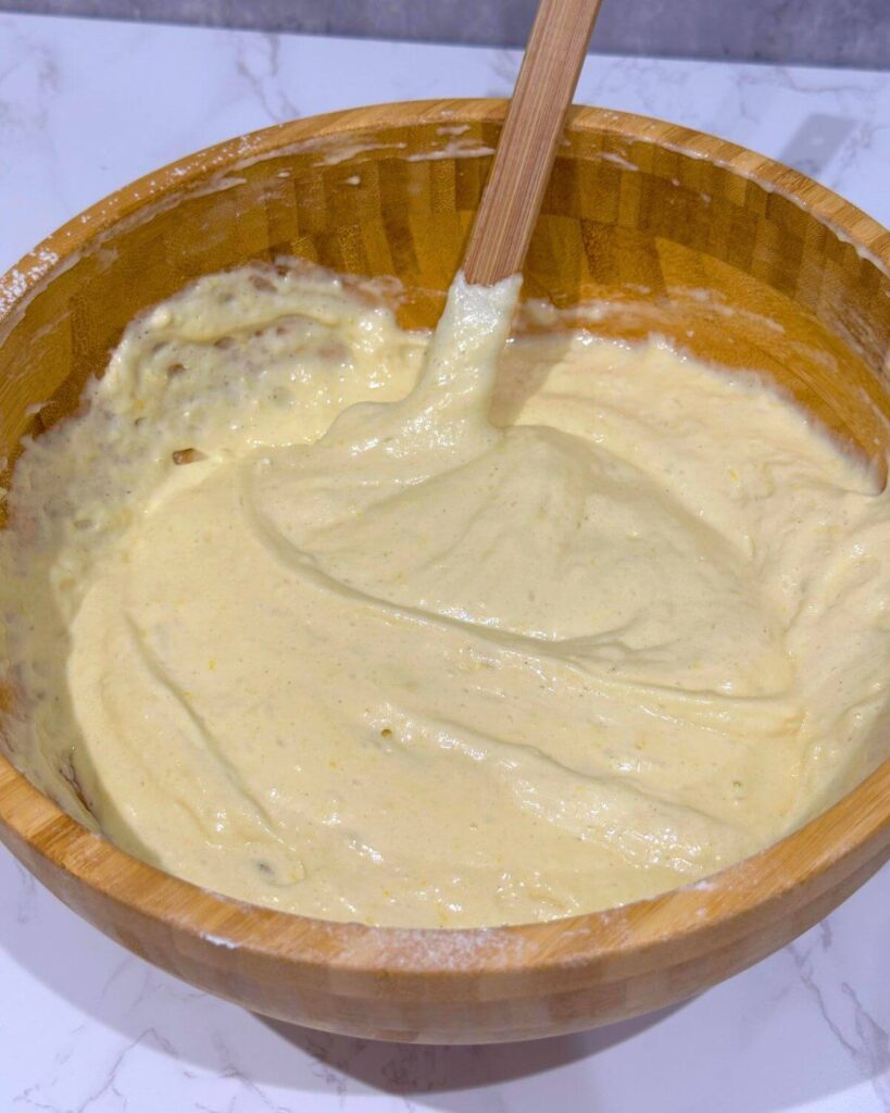 A wooden mixing bowl filled with a fluffy, light batter and a spatula inside. 