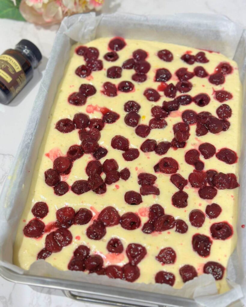 Baking tray filled with batter and cherries pressed into the top, ready to be baked.