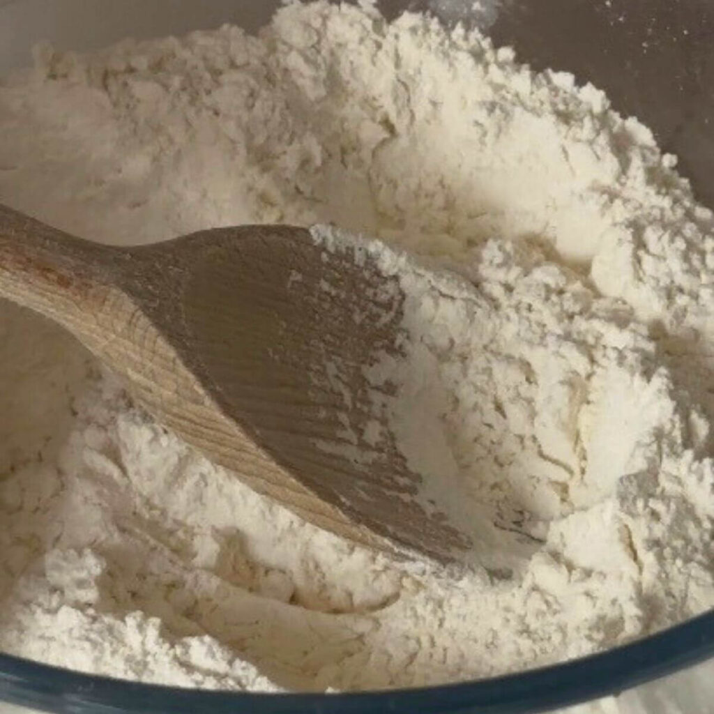 A clear bowl filled with all the dry ingredients for chocolate chip cookies: all-purpose flour, baking soda, baking powder, kosher salt, ready to be mixed.