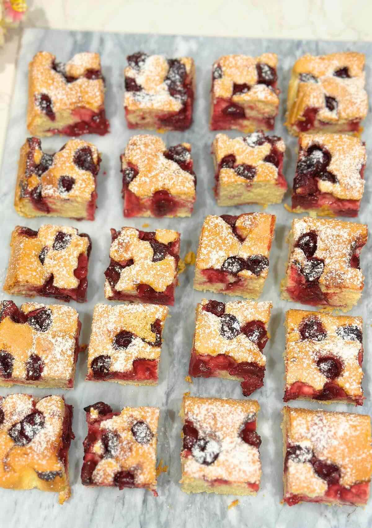 Squares of Morello Cherry Sponge Cake displayed on a marble surface, showcasing the moist center filled with juicy cherries.