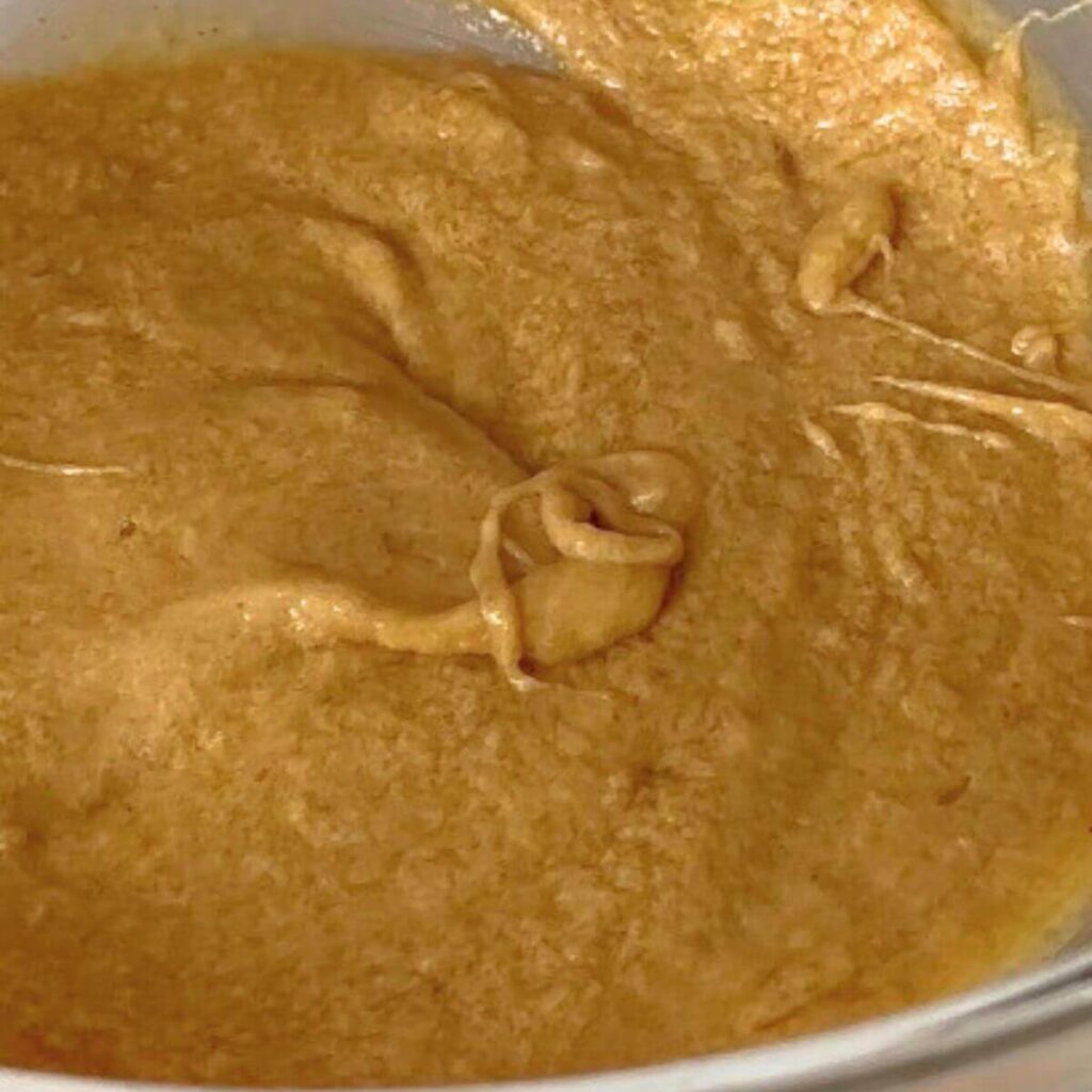 A mixing bowl filled with a smooth mixture of melted butter, light brown sugar, white granulated sugar, vanilla extract, and a large egg, prepared for chocolate chip cookies.