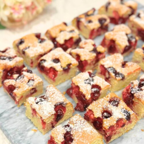 Squares of Morello Cherry Sponge Cake displayed on a marble surface, showcasing the moist center filled with juicy cherries.