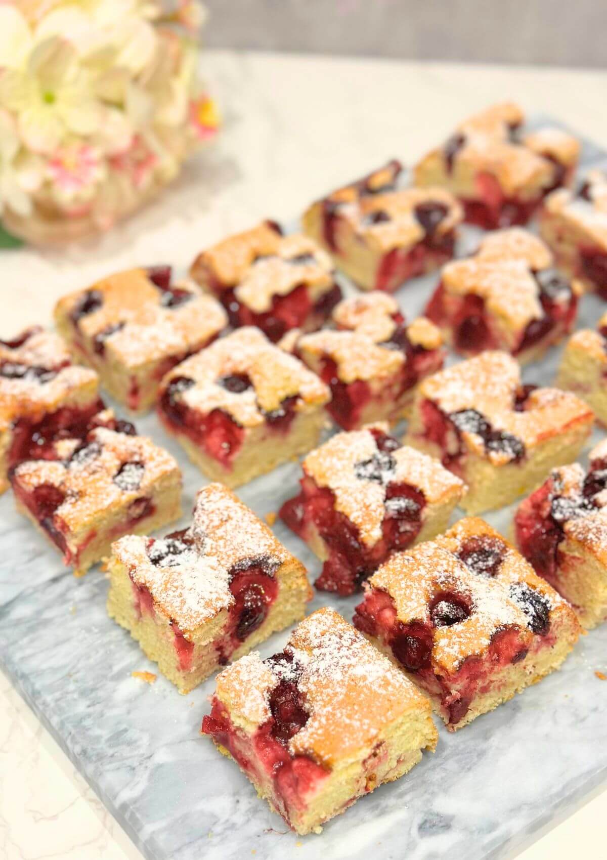 Squares of Morello Cherry Sponge Cake displayed on a marble surface, showcasing the moist center filled with juicy cherries.