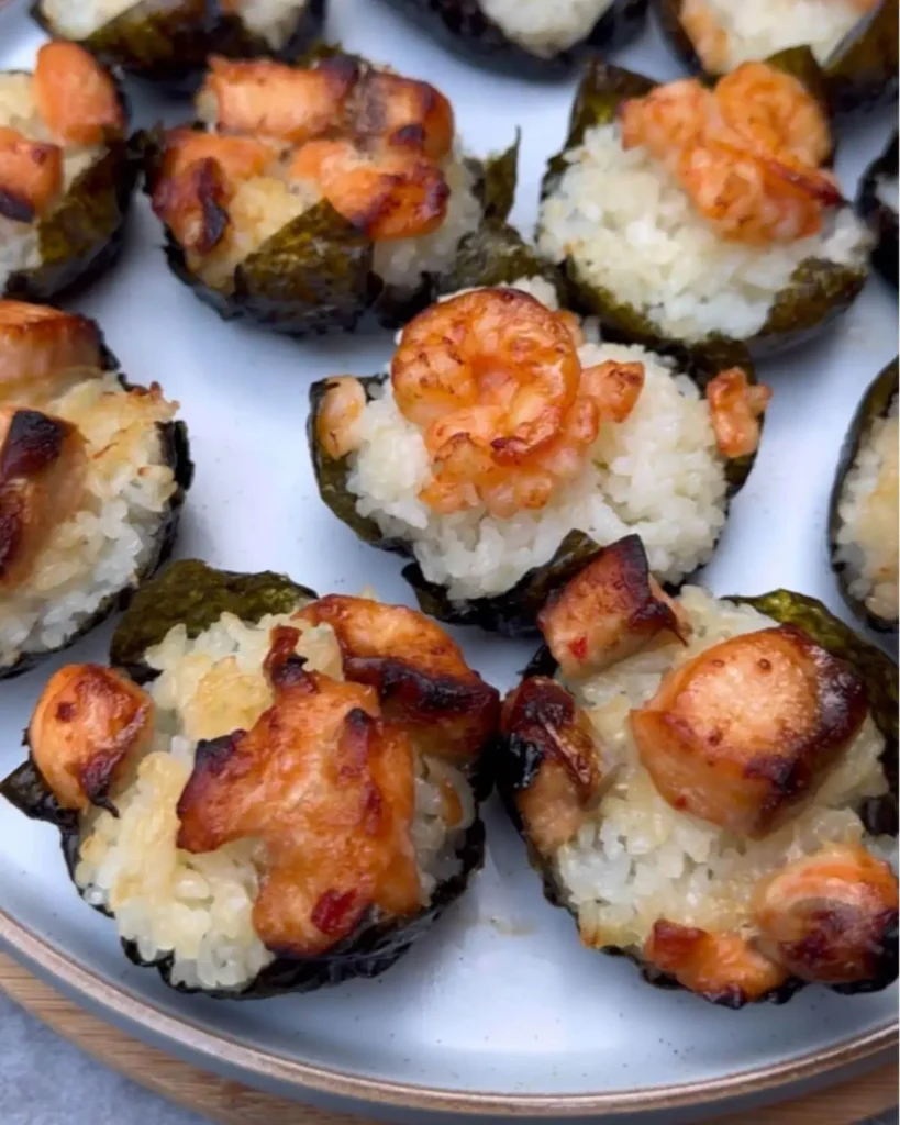 Freshly baked sushi cups with crispy nori edges, topped with perfectly cooked salmon and prawns, ready to be garnished with avocado, sesame seeds, and green onions.