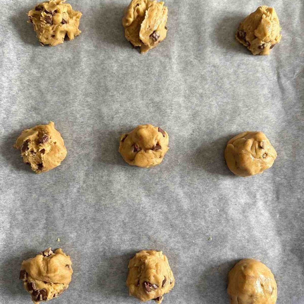 Chocolate chip cookie dough shaped into balls, placed on a baking sheet, ready to be baked into delicious cookies.