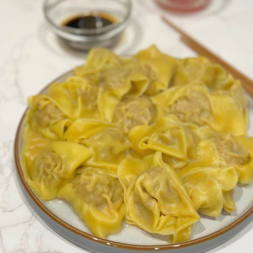 Light and tasty turkey wontons on a plate, accompanied by small bowls of soy sauce and chili sauce, with wooden chopsticks nearby.