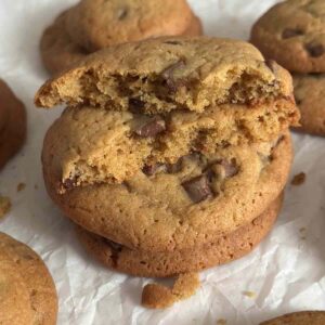 A stack of chewy biscuits forming a tower, with one cookie split in half to reveal its soft, gooey center, surrounded by more cookies scattered around the tower.