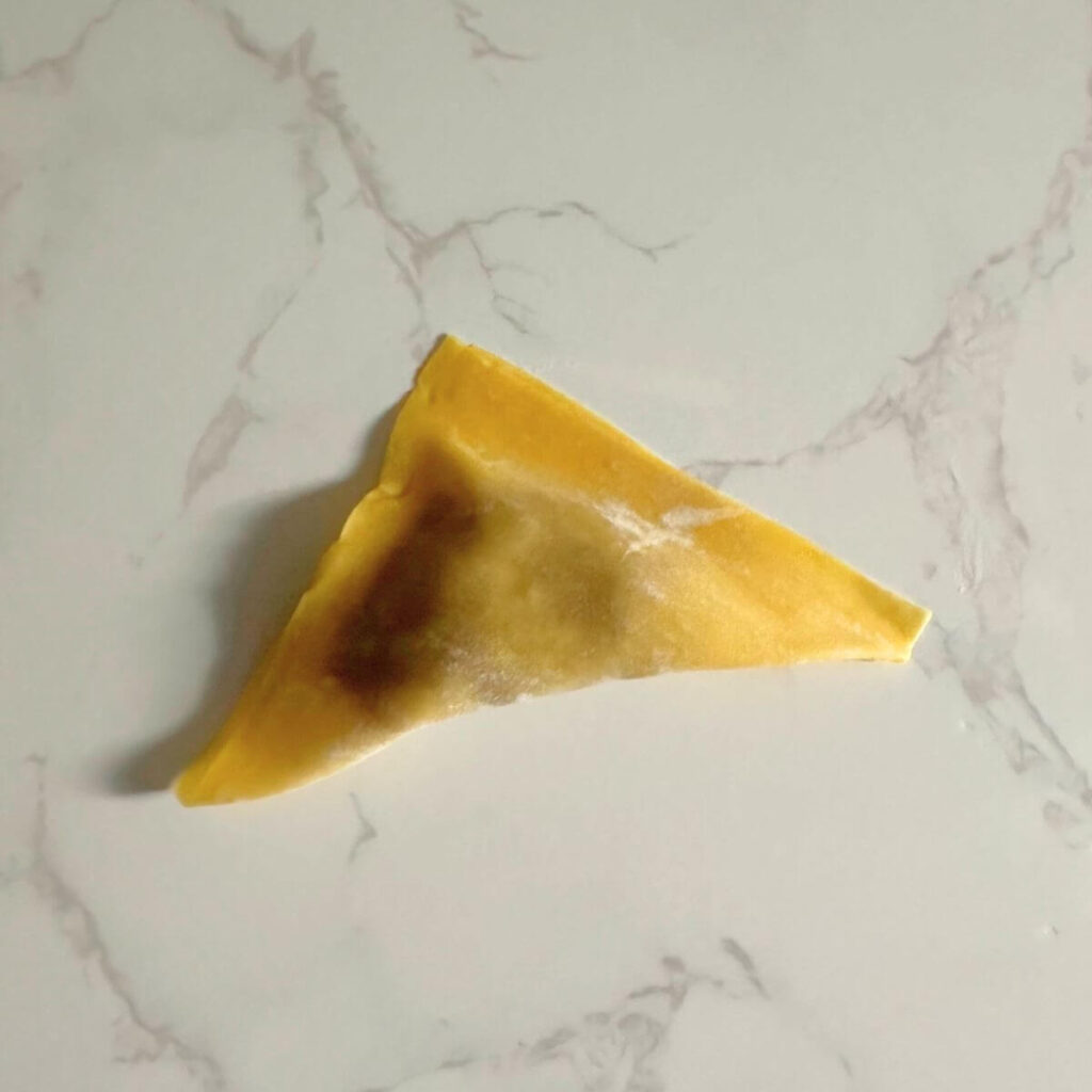 Folding turkey wontons: a squared wonton pastry with a small amount of filling in the center, sealed into a triangle shape on a surface.