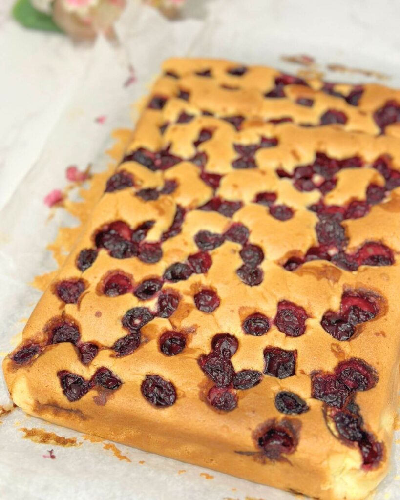  Golden brown baked cake, with cherries visible on top, ready to be sliced into portions.