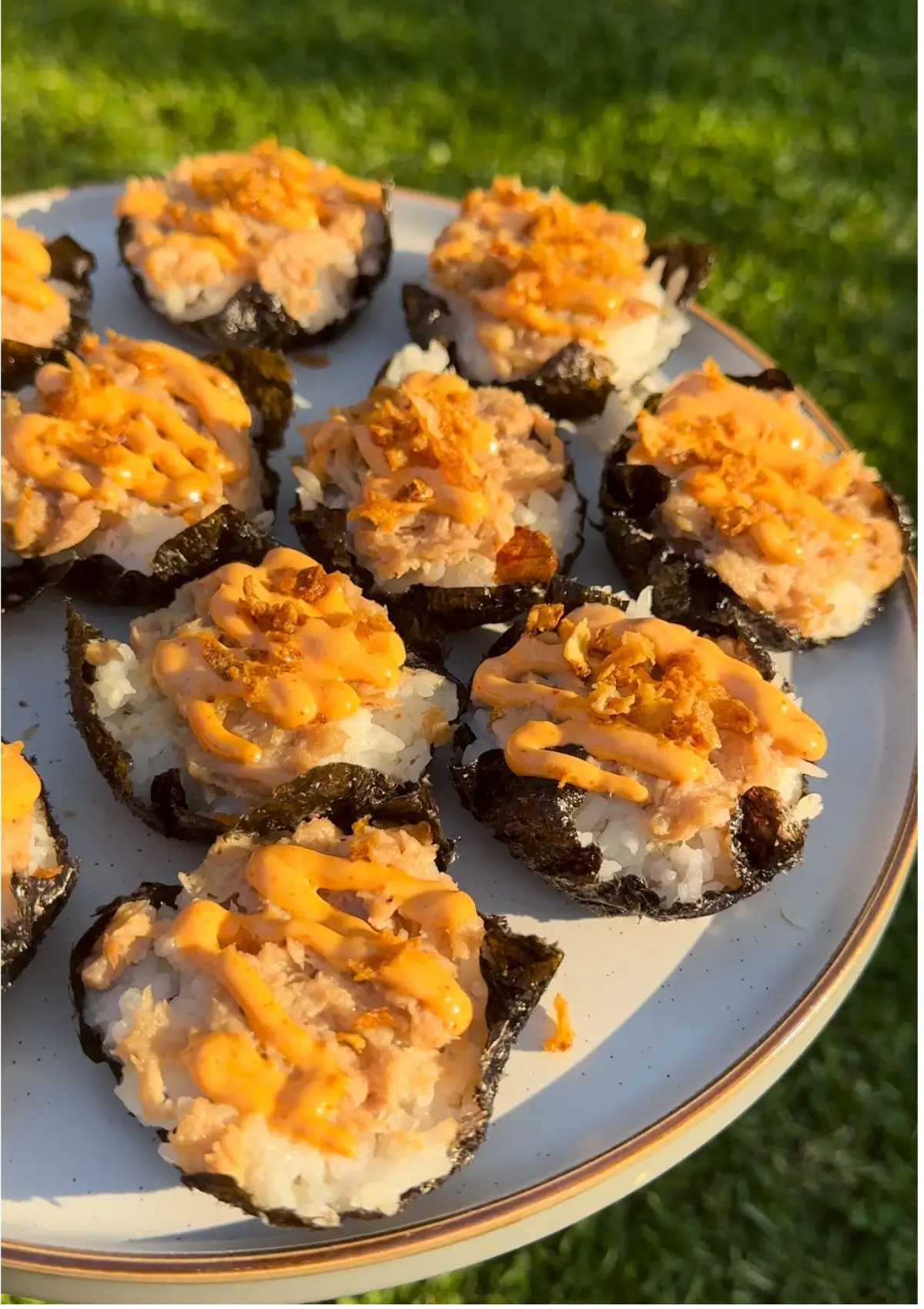 Baked tuna sushi cups topped with sriracha mayo and sprinkled with onion flakes on a round plate.