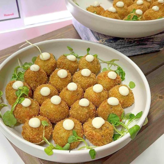 Cheese balls in a white shallow bowl, garnished with microgreens, each topped with a drop of white dressing.