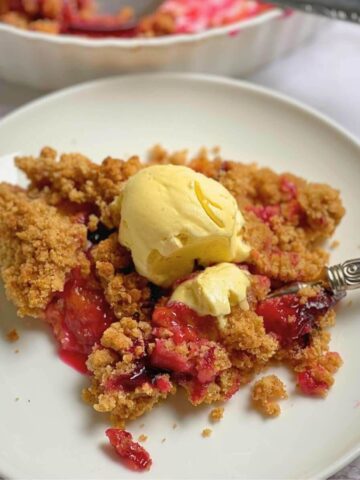 Plum crumble on a plate with a scoop of vanilla ice cream.