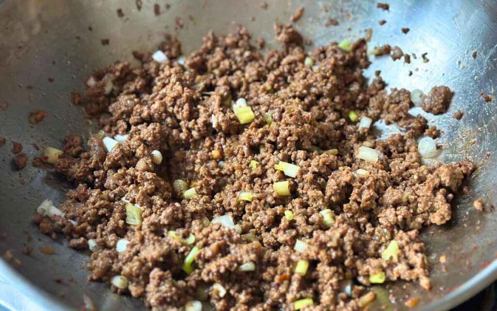 Ground beef tacos filling in a pan, garnished with green onions. 