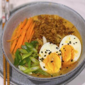 Miso noodle soup with boiled egg, onion flakes, green onions, carrot strings, sesame seeds, and chilli oil.