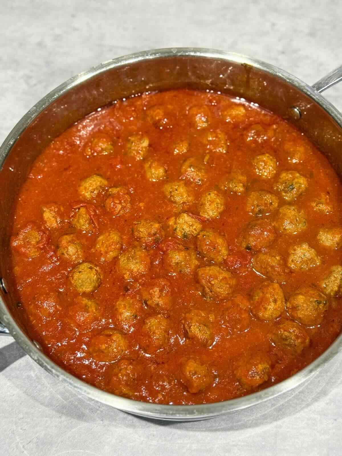 Meatballs in marinara sauce in a stainless steel pan.