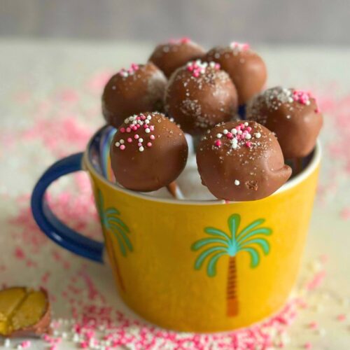 Pistachio Cake Pops in a yellow cup surrounded by sprinkles, one cake pop has a bit take out to see the interior