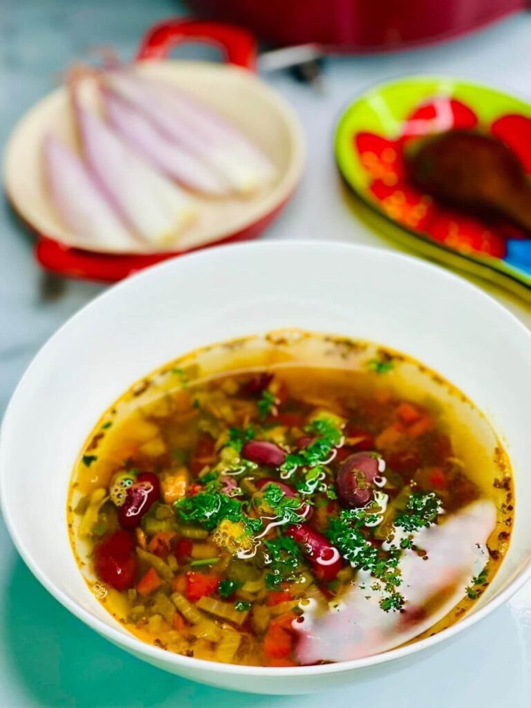 Traditional Romanian Bean Soup (Ciorba De Fasole) served in a bowl with onions in the background.