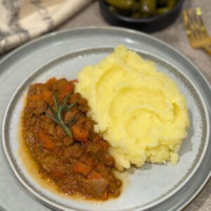 One-Pan Beef Stew with Veggie Mash on a grey plate with pickled cucumbers in the background.