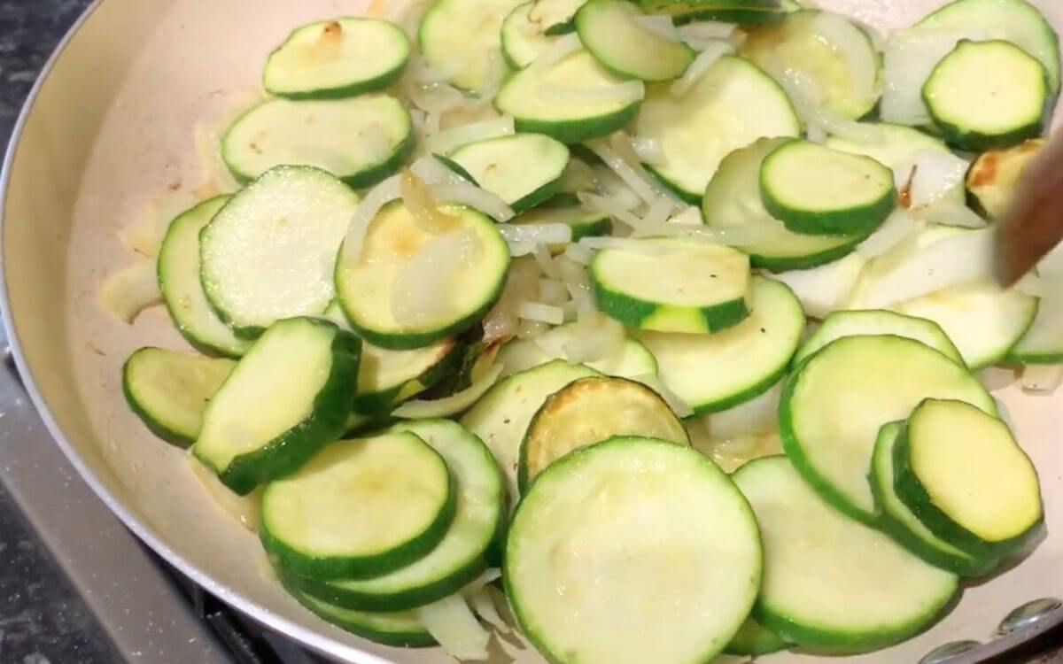 Softened zucchini and onions in a pan after sautéing.