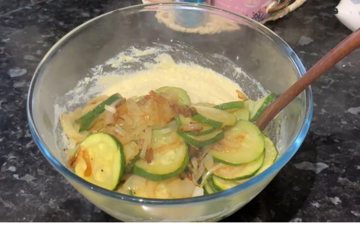 Stirring cooked zucchini and onion into the batter until well combined.