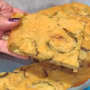 A square of zucchini scarpaccia is held in my hand, showing its crispy edges and soft centre.