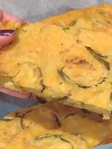 A square of zucchini scarpaccia is held in my hand, showing its crispy edges and soft centre.